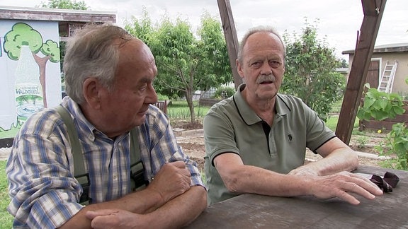Männer sitzen an einem Gartentisch im Gespräch.