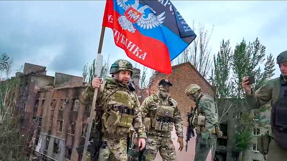 Auf diesem Foto aus einem Video, das von Denis Puschilin, Chef der teils von Russland besetzten Region Donezk, veröffentlicht wurde, hält Denis Puschilin eine Fahne der russisch kontrollierten Region Donezk auf einem beschädigten Gebäude in Bachmut. 