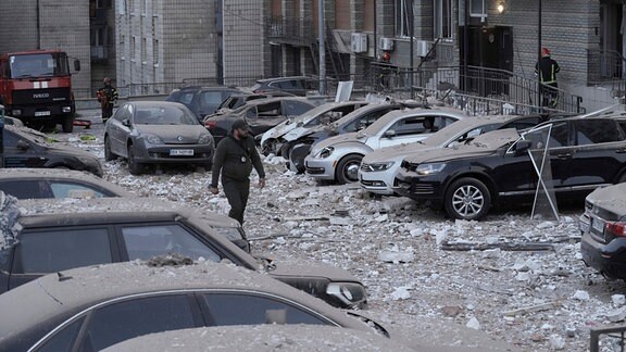 Ein Polizist geht auf dem Parkplatz mit beschädigten Autos vor einem mehrstöckigen Wohnhaus spazieren, das bei einem russischen Angriff in Kiew.
