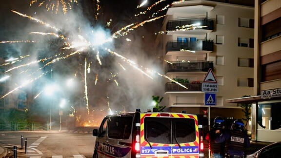 Polizisten neben Polzeifahrzeug, im Hintergrund Feuerwerk