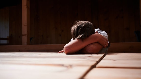 ILLUSTRATION - Ein Kind versteckt sein Gesicht unter seinen Armen und liegt mit dem Kopf auf einem Tisch. (gestellte Szene)