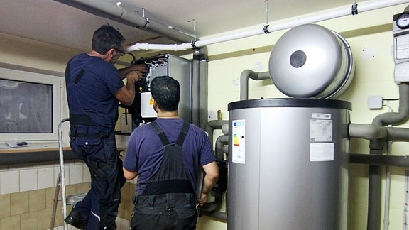 Zwei Handwerker bei der Einrichtung einer Wärmepumpe im Keller eines Hauses.