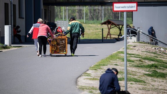 Menschen schieben einen Wagen mit Spielzeug über das Gelände der Erstaufnahme-Einrichtung (EAE) des Landes Brandenburg in Eisenhüttenstadt. 