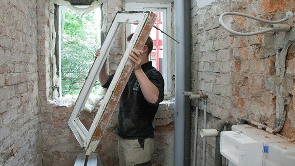 Ein Arbeiter baut ein altes Fenster aus.