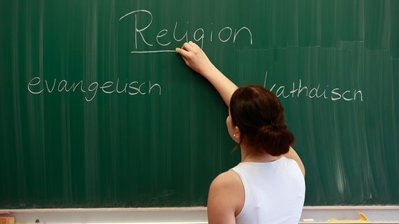Symbolbild: Schülerin schreibt an die Tafel: Religion
