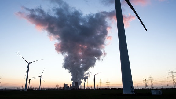 Windräder stehen 2020 vor dem Braunkohlekraftwerk Niederaussem während die Sonne untergegangen ist.