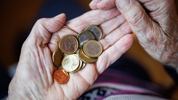 Eine ältere Dame zählt in ihren Händen das Bargeld aus ihrem Portemonnaie ab.