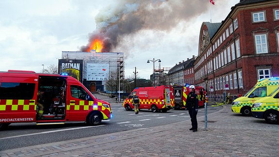 Feuer und Rauch steigen aus der Alten Börse, "Boersen" bei einem Brand in Kopenhagen. Davor eine Absperrung der Polizei.
