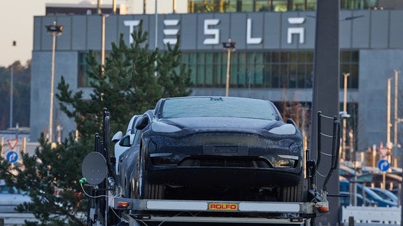 Ein Tesla-PKW steht am frühen Morgen vor der Tesla-Autofabrik auf einem Transporter.