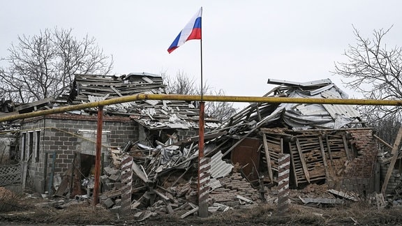 Eine russische Fahne weht vor einem zerstörten Gebäude