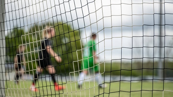 Spielerinnen sind während eines Fußballspiels hinter dem Netz eines Tors zu sehen. 