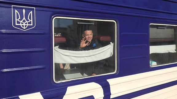 Ein Junge winkt lächelnd aus einem Zug.