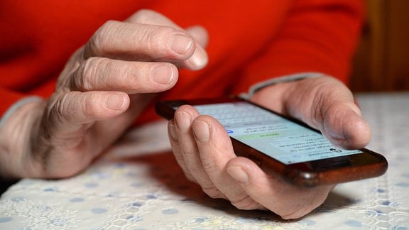 Ältere Frau hält Smartphone in der Hand und will mit der anderen darauf tippen. 