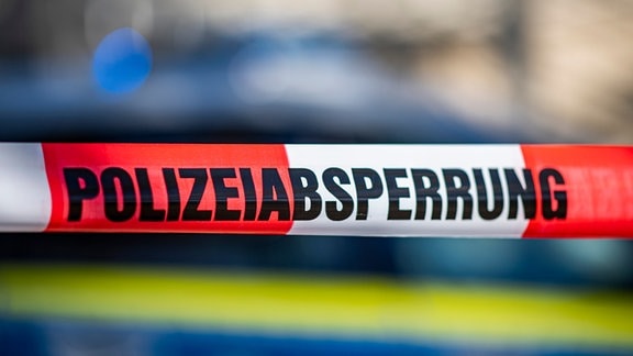 Ein Absperrband mit der Aufschrift «Polizeiabsperrung» ist vor einem Polizeiwagen aufgespannt.