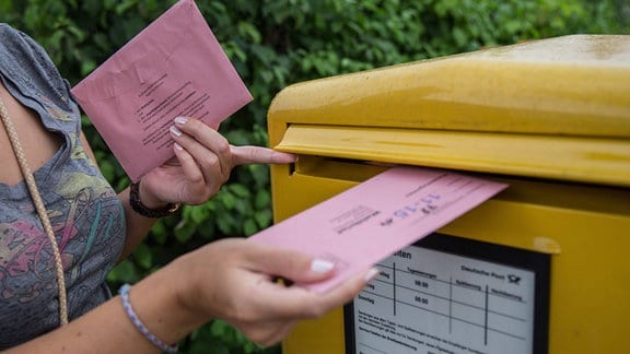 Eine Person wirft ihre Briefwahlunterlagen in den Postkasten der Deutschen Post