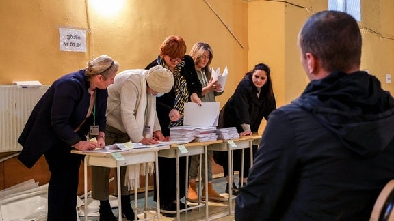 Eine Person beobachtet eine Gruppe beim auszählen von Wahlzetteln.