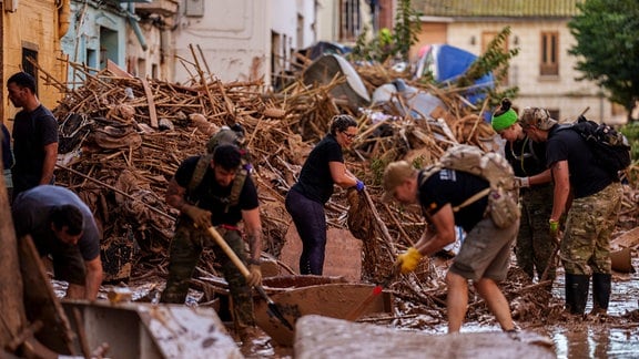 Menschen schaufeln Schlamm weg und versuchen eine Straße in Valencia zu reinigen