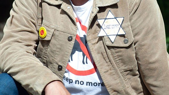 Zwei Demonstranten sitzen auf Steinstufen, der linke Demonstrant, männlich, hat einen Judenstern auf der Jacke auf diesen steht Ungeimpft .