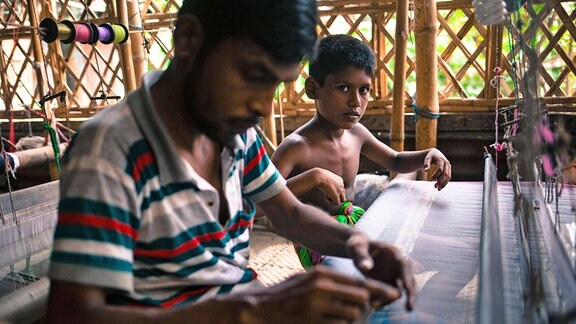 Ein Mann und ein Junge an einem Webstuhl in einem Textilbetrieb in Bangladesh