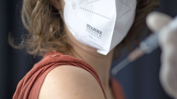 Junge Frau mit FFP2 Maske wird geimpft.