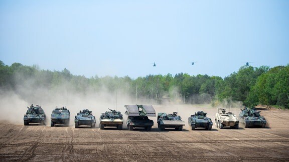 Panzer und Hubschrauber auf einem Übungsfeld in Aktion.