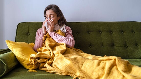 Frau mit Erkältung, eingemummelt auf dem Sofa