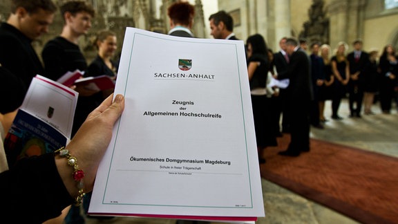 Jemand hält ein Zeugnis der Allgemeinen Hochschulreife des Ökumenischen Domgymnasiums Magdeburg in einer Hand.