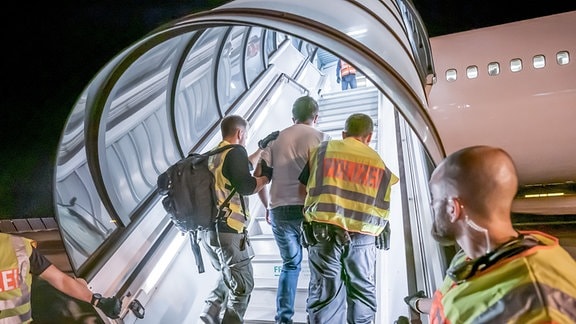 Polizeibeamte begleiten zwei Personen auf dem Flughafen Leipzig-Halle in ein Charterflugzeug.