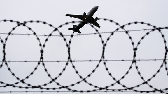 Ein Flugzeug von Lufthansa startet am Flughafen Hannover - fotografiert durch Stacheldraht am Flughafenzaun.