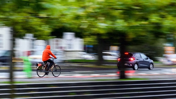 Ein Mann fährt mit einem Fahrrad am frühen Morgen neben einem Auto durch die Innenstadt.