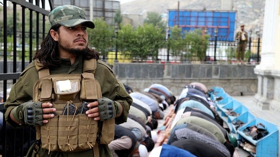 Afghanen verrichten das Eid al-Fitr-Gebet, während ein Taliban-Kämpfer in einer Moschee in Kabul, Afghanistan, Wache steht.