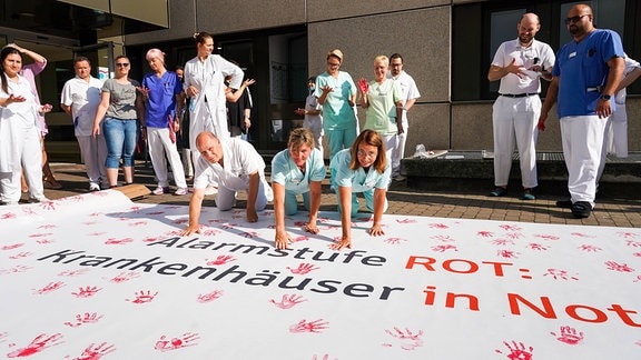 Mitarbeiter der Kreisklinik Groß-Gerau drücken ihren Protest anhand eines Plakats mit roten Händen aus