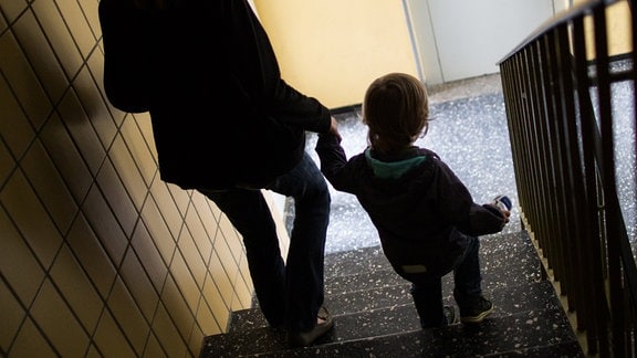 Eine alleinerziehende Mutter geht 2016 mit ihrem Sohn durch einen Hausflur die Treppe herunter.