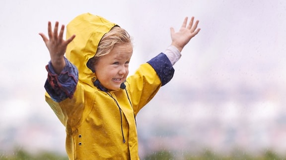 Ein Kind steht im Regen mit gelber Regenjacke.