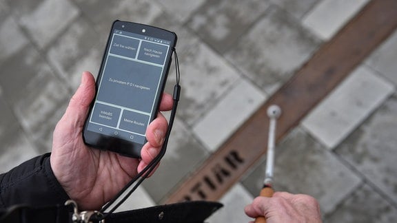 Eine blinde Person hält ein Smartphone mit der Verkehrs-App "InMoBS" in der Hand. 