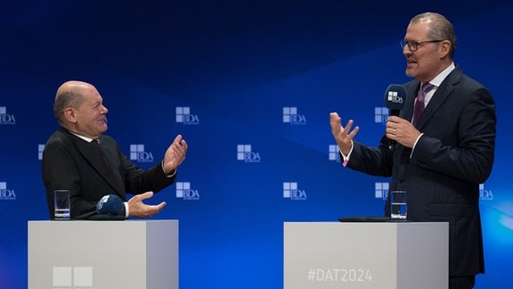 Bundeskanzler Olaf Scholz (SPD, l) spricht während des Deutschen Arbeitgebertages 2024 der Bundesvereinigung der Deutschen Arbeitgeberverbände (BDA) mit Rainer Dulger, Präsident der Bundesvereinigung der Deutschen Arbeitgeberverbände.