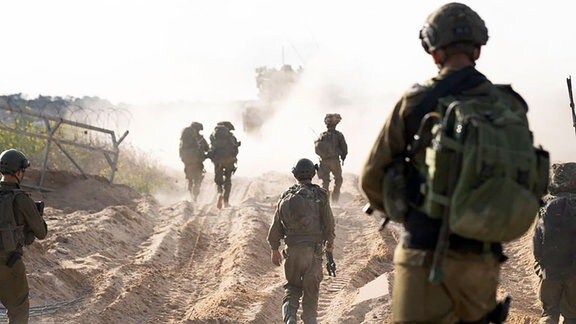Soldaten in Kampfmontur laufen über einen staubigen Untergrund