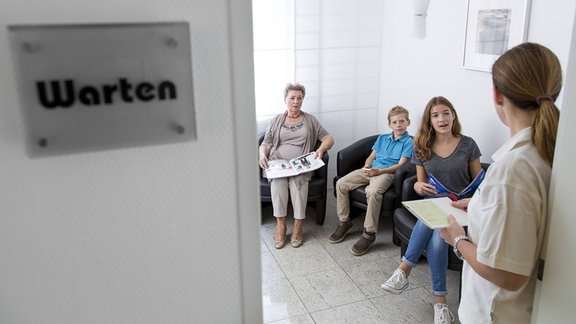 Sprechstundenhilfe ruft in einem Wartezimmer einen Patienten auf.