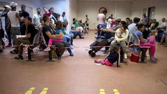 Asylsuchende warten vor einer gelben Markierung im Warteraum auf ihre Wartenummer in der Zentralen Aufnahmeeinrichtung des Landes Berlin fuer Asylbewerber, ZAA, in Berlin Tiergarten. -