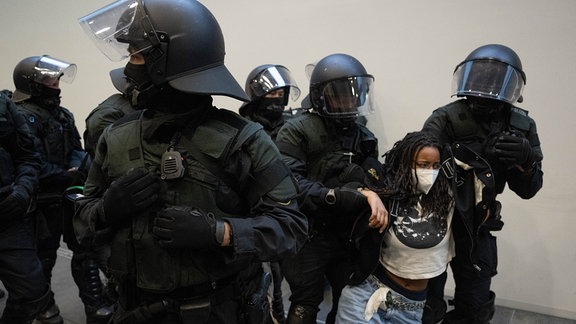 Polizisten tragen vor dem besetzten Audimax der Universität Leipzig eine Frau aus dem Gebäude.