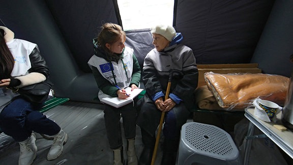 Ältere Frau wird in Sumy in einer Aufwärmstation durch Caritas-Mitarbeiterin betreut.