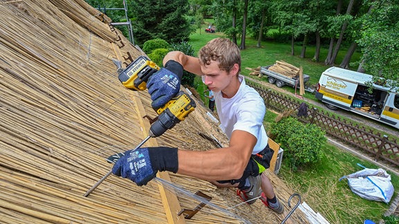 Pascal Herold, angestellter Dachdecker bei Dachdeckermeister Daniel Girke, arbeitet auf einem Reetdach eines Hauses im Spreewald.