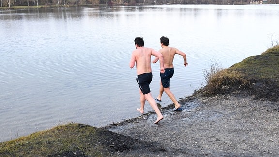 Zwei Männer in Badehosen gehen in einen See.