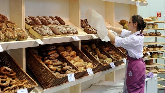 Eine Bäckereifachverkäuferin greift nach einem Brot ins Regal