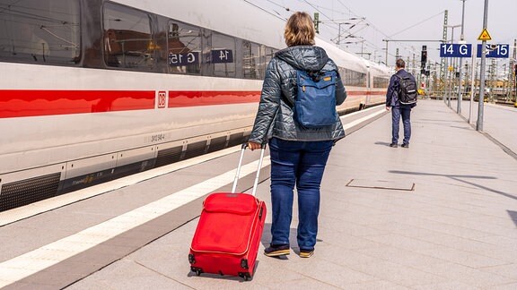 Bahnkundin mit Gepäck am Bahnsteig vor einfahrendem ICE