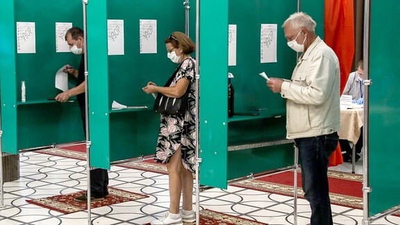 Menschen beim Wählen in den Wahlkabinen.