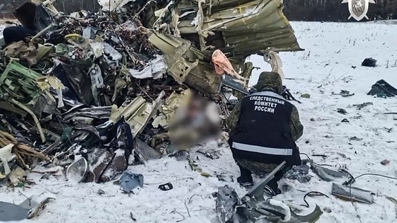 Ein Mann hockt vor den Trümmern einer abgestürzten Ilyushin Il-76.