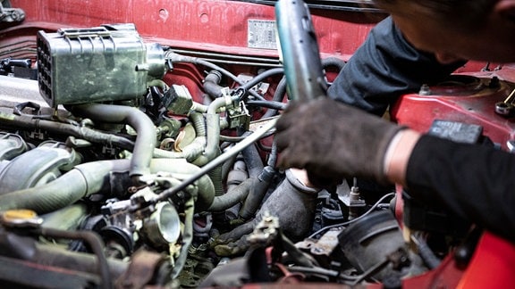 Die Hände eines Automechanikers arbeiten im Motorraum eines Autos.