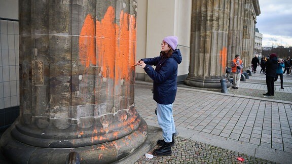 Zwei Klimaaktivistinnen bemalen das Brandenburger Tor mit oranger Farbe.