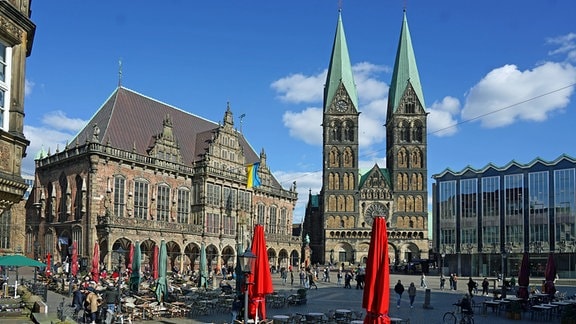 Frühlingsnachmittag auf dem Bremer Marktplatz. Links das Rathaus mit Ukraine-Flagge, in der Mitte der Sankt-Petri-Dom, rechts das Haus der Bürgerschaft. 